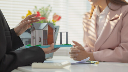 Inside a real estate office a real estate agent is using a house mockup to present the design and...