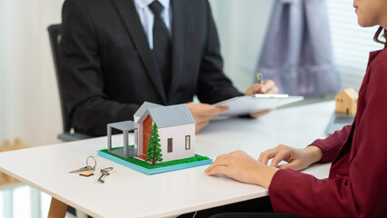 Inside a real estate office a real estate agent is using a house mockup to present the design and promotions that the client will receive when they sign sales contract. Real estate investment concept