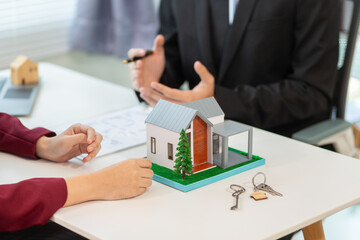 Inside a real estate office a real estate agent is using a house mockup to present the design and promotions that the client will receive when they sign sales contract. Real estate investment concept