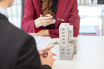 Inside a real estate office a real estate agent is presenting a condominium unit for sale to a client and offering a valuable promotion to entice the client to purchase their own property. copy space