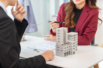 Inside a real estate office a real estate agent is presenting a condominium unit for sale to a client and offering a valuable promotion to entice the client to purchase their own property. copy space