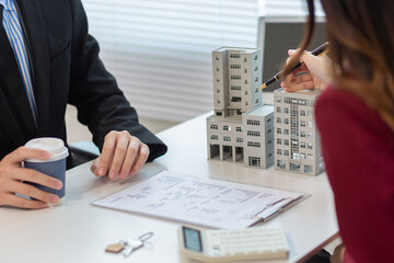 Inside a real estate office a real estate agent is presenting a condominium unit for sale to a client and offering a valuable promotion to entice the client to purchase their own property. copy space