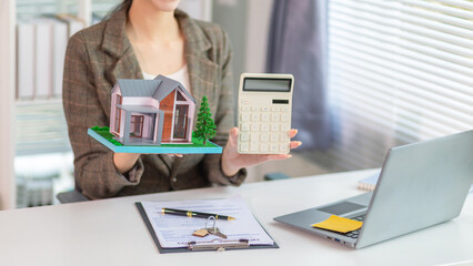 Inside a real estate office a real estate agent is using a house mockup to present the design and promotions that the client will receive when they sign sales contract. Real estate investment concept