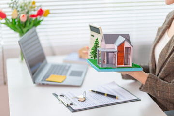 Inside a real estate office a real estate agent is using a house mockup to present the design and promotions that the client will receive when they sign sales contract. Real estate investment concept