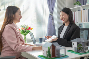 Inside a real estate office a real estate agent is using a house mockup to present the design and...