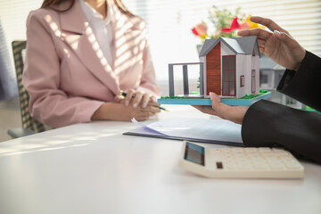 Inside a real estate office a real estate agent is using a house mockup to present the design and...
