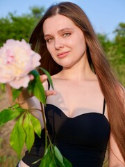 Naklejka premium Happy smiling woman outdoors with pink peony flowers enjoying life in the moment at sunset