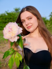 Naklejka premium Happy smiling woman outdoors with pink peony flowers enjoying life in the moment at sunset