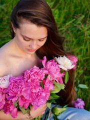 Happy smiling young woman in summer outdoors in a field with pink peony flowers enjoying life in a moment at sunset