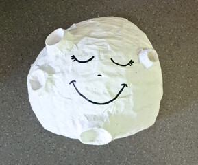 white paper mache moon with smiling, sleeping face drawn on