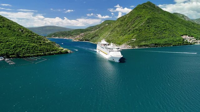 Aerial drone view of a cruise liner near the town of Perast, located in the Bay of Kotor. Tourist boats are sailing nearby. The island of Saint George is visible on the horizon. Montenegro, Europe.