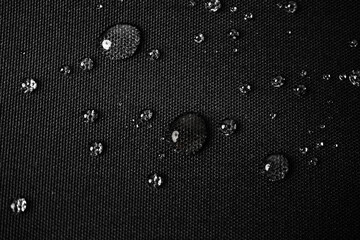 Close-up of water droplets beading on a black waterproof fabric surface, showcasing water...