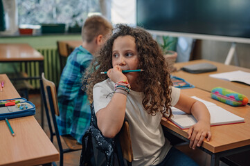 Elementary school student chewing on pencil while thinking in classroom
