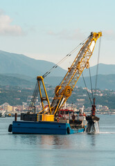 Fototapeta premium Floating crane dredger with grab bucket working in harbor