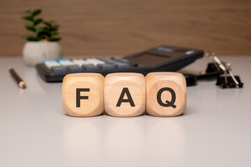 wooden cubes with letters FAQ on desk near calculator