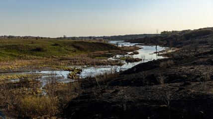 A Beautiful Spring Landscape Featuring Burnt Grass Alongside a Serene River in a Picturesque Setting