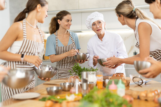 Elderly woman cook at master class teaches group of woman how to cook food