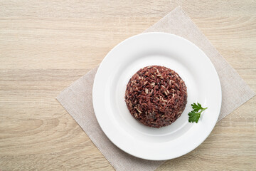 Cooked brown rice or riceberry rice on white plate on wood table