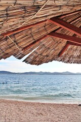 umbrella on an empty beach, natural umbrellas, sand on the beach, straw umbrella, Zadar, Croatia