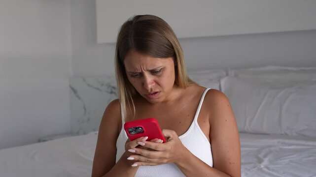 Young blonde woman touches lymph nodes on her neck, looking worried. She holds a phone, searching for health symptoms. Anxiety, hypochondria, fear of illness, self-awareness