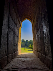Stone arch window opening to a peaceful garden. Framed view of green nature, trees, and soft grass,