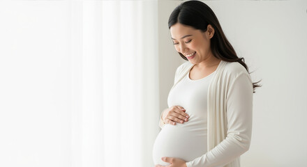 Smiling pregnant asian woman touching belly in white outfit. Maternity pregnancy expecting mother prenatal care wellness family planning motherhood baby love