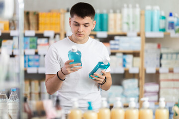 Guy chooses a mouthwash in a pharmacy against the background of racks with medicines and vitamins