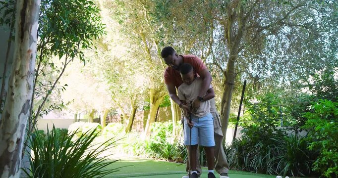 African American father pointing out putter features and teaching son putting on yard green
