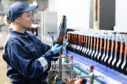 Female worker inspecting beer bottles on production line in brewery factory - Powered by Adobe