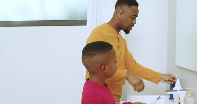 African American father and son rinsing, applying paste, brushing in circles at sink at night