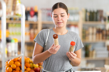 Fototapeta premium Young woman buyer chooses seasoning herbs in jar in grocery store