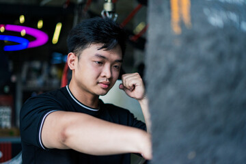 Young Asian man training at a boxing gym while punching a heavy bag in an urban setting during daytime