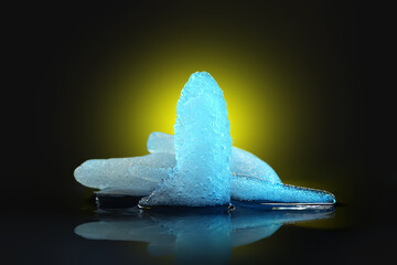 Ice melting. Pieces of melting ice on a dark background. Colored blue yellow backlight. Selective focus