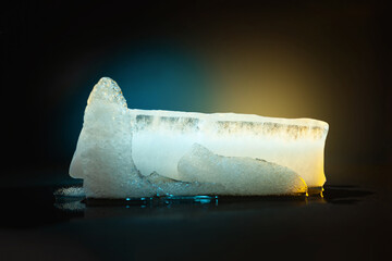 Ice melting. Pieces of melting ice on a dark. Colored blue yellow backlight