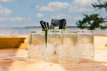 Table de restaurant ou de camping avec des verres posée sur une table en bois face a la mer