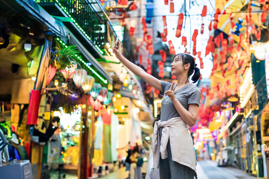Woman enjoying local culture while exploring vibrant alley filled with lanterns and decorations during evening hours in an Asian market