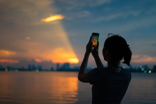 Individual captures sunset reflection over water with smartphone in urban setting during evening hours - Powered by Adobe