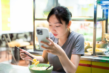Young woman enjoys meal while using smartphone in a casual dining setting during daytime