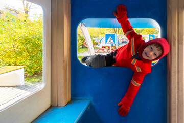 Child with red raincoat of firefighter clings to a rope in a playground during rain. High quality photo