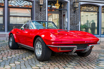 red classic american sportscar in front of historical building