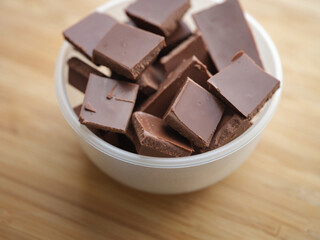 A heap of broken milk chocolate in a bowl. Shallow depth of field. Close up.