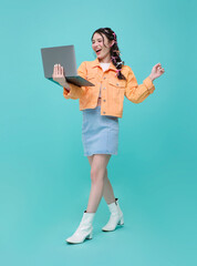 Full length Happy young beautiful Asian business woman using laptop While her walking isolated on blue background.
