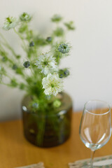 a bouquet of daisies in a glass vase stands on a table on a white background, a wine glass on the table, depth of field, side effect, defocus, macrophotography, bokeh