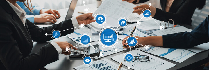 A diverse business team engages in collaborative analytic discussions using laptops and documents. Modern technology enhances their strategic meeting in an office environment. Amity