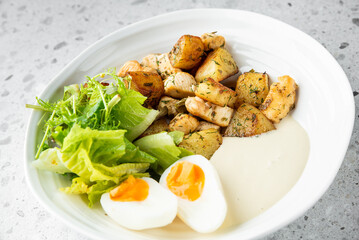 A nutritious dish featuring roasted potatoes, grilled chicken, fresh green salad, and a soft-boiled egg with a creamy sauce, served on a white plate. Perfect for healthy eating and balanced meals
