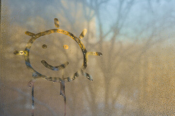 drawing of the sun on wet glass. Cheerful sun painted on fogged glass creates optical illusion of...