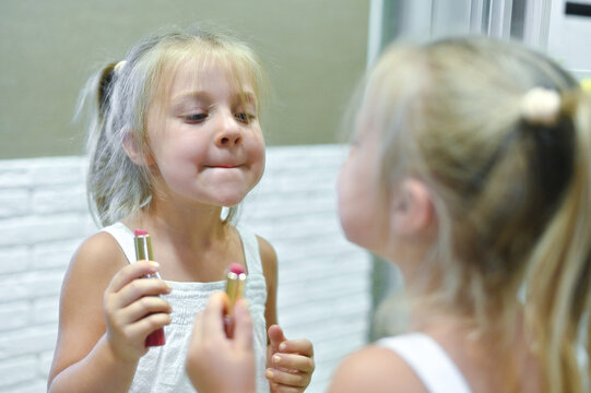 a little girl paints her lips in front of a mirror with her mother's lipstick.
