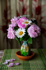 June bunch of pink roses and white daisies in tiny vase indoors. Tender pink petals of roses fell from the flowers to the table. Floral still life.