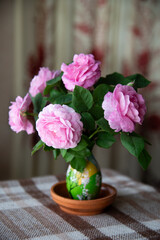 June bunch of pink roses in tiny vase indoors. Tender pink petals of roses fell from the flowers to the table. Floral still life.