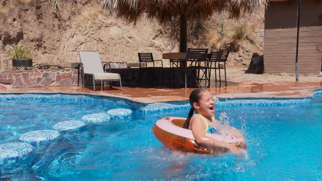una ni&ntilde;a peque&ntilde;a con un inflable y traje de ba&ntilde;o saltando a la alberca feliz y disfrutando de unas vacaciones de verano saltando en el agua fria en la naturaleza